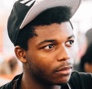 Small profile picture of a young black man in a baseball hat looking to the right.